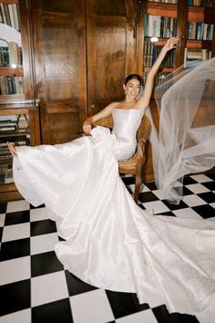 a woman in a white wedding dress sitting on a chair with her arms up and legs spread out