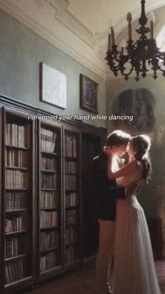 a man and woman are kissing in front of bookshelves with chandelier