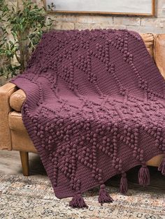 a couch with a blanket on top of it in front of a brick wall and potted plant