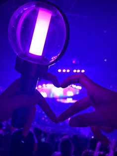 two hands making a heart shape with their fingers in front of a purple light at a concert