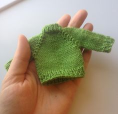 a hand holding a small green knitted sweater in it's left palm area