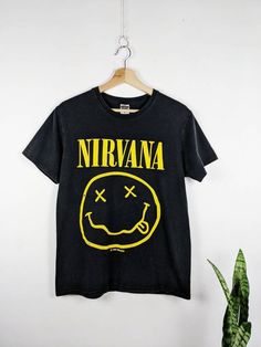 a black nirvana t - shirt hanging on a wall next to a potted plant