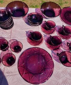 a table topped with lots of purple dishes and bowls on top of a white cloth