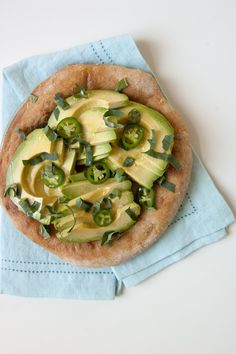 an avocado pizza is sitting on top of a blue napkin with green peppers and jalapenos