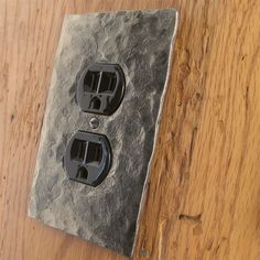 an electrical outlet cover with two black outlets on top of it and a wood floor