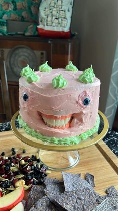 a pink cake with green icing and an apple on the side next to crackers