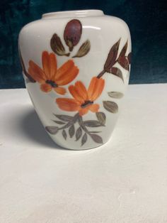 a white vase with orange flowers and leaves painted on the side, sitting on a table