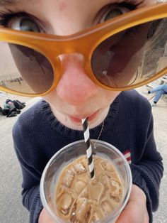 a young boy wearing sunglasses and drinking from a plastic cup with a straw in it