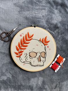 a cross stitch pattern with a skull and orange leaves on it, next to scissors