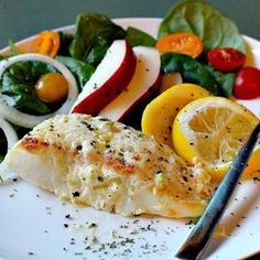 a white plate topped with fish and veggies next to a knife and fork