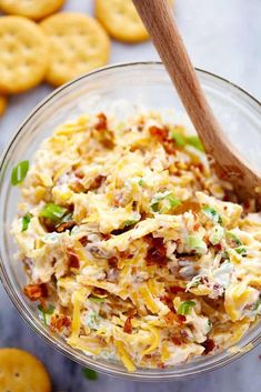 a glass bowl filled with chicken salad next to crackers on the side and a wooden spoon in it