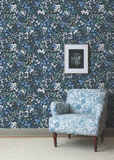 a blue chair sitting in front of a wall with flowers on it