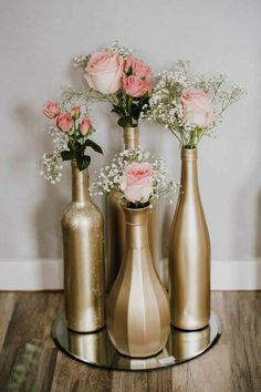 three gold vases with flowers in them on a wooden floor next to a wall