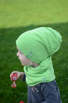 a small child wearing a green hat and holding a red object in his hand while standing on some grass