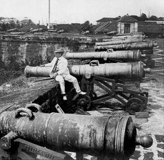 an old black and white photo of a man sitting on a cannon