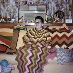 a woman is sitting on a couch covered in blankets and crocheted afghans