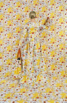 a woman standing in front of a yellow and white wall with an orange handbag