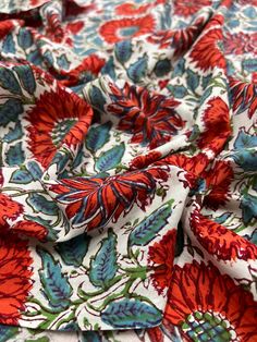 an orange and blue flowered fabric with green leaves on it, as well as red flowers