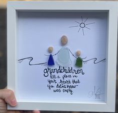 a person holding up a white frame with three stones in it and the words grandmother written on it