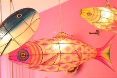 three colorful fish hanging from strings in a pink room with other decorations on the wall