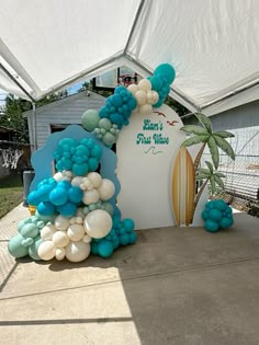 a white and blue balloon arch with palm trees on the side under an awning