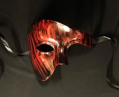 This Phantom mask is hand painted in a sold black then brushed red to give an abstract look. Mask is fully sealed and has a nice gloss look, Great for any Masquerade event or mask costume party! Size 6.5"W x 5.5"H. Color red and black. Fire Themed Masquerade Mask, Red Masquerade Mask Men, Red Mask Aesthetic, Black Masks For Halloween Gift, Black Halloween Masks As Gifts, Red Eye Mask For Mardi Gras, Red Masks And Prosthetics For Mardi Gras Masquerade, Red Venetian Eye Mask, Red Eye Mask As A Gift