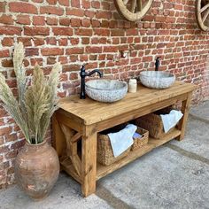 two sinks are sitting next to each other in front of a brick wall and some plants