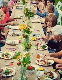 a group of people sitting at a long table eating food and drinking water from glasses