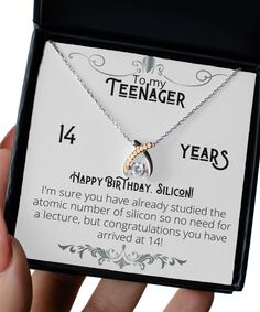 a person holding up a birthday card with a diamond pendant on it's neck