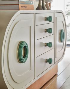 a white cabinet with green handles and knobs on the front, next to a bookshelf