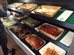 a woman standing in front of a display case filled with lots of different types of food