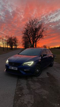 a blue car parked on the side of a road under a pink sky with clouds