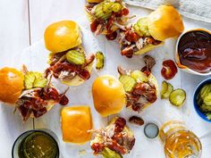 pulled pork sliders with barbecue sauce and pickles on a cutting board next to dipping sauces