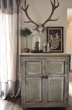 an old dresser with antlers on it in front of a painting and window sill