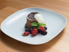 a piece of chocolate cake with whipped cream and berries on a white plate sitting on a wooden table