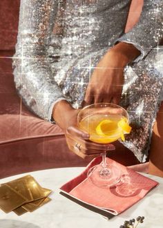 a woman is holding a cocktail glass with an orange peel in it on a table