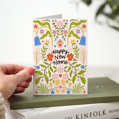 a hand holding up a card that says happy new home with flowers and plants on it