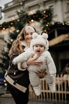 a woman holding a baby in front of a christmas tree with lights on the trees