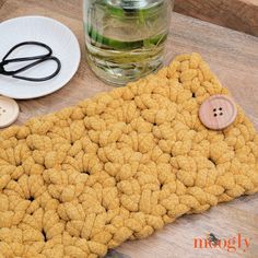 a crocheted place mat with buttons on it next to a glass of water