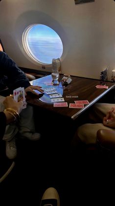 two people sitting at a table with playing cards in front of an airplane window that looks out onto the ocean