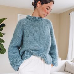 a woman wearing a blue sweater and white pants in front of a couch with a potted plant