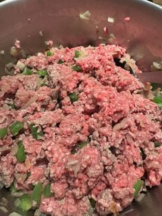 a large metal bowl filled with meat and green onions on top of a wooden table