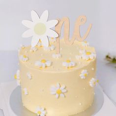 a yellow cake with white flowers on top and the word me spelled in wooden letters