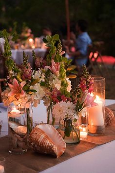 a table topped with vases filled with flowers and seashells next to candles