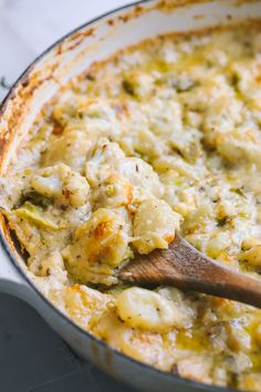 a casserole dish with broccoli and cheese being stirred by a wooden spoon