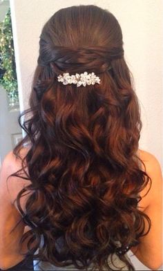 the back of a woman's head with long curly hair and flowers in her hair