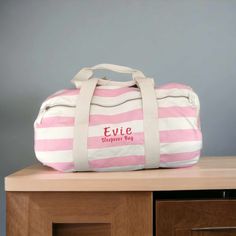 a pink and white striped duffle bag sitting on top of a wooden dresser next to a gray wall