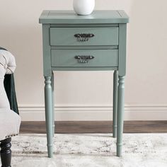 a blue table with two drawers and a white vase on top, in front of a chair