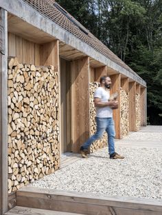 a man standing in front of a pile of logs next to a building with wooden walls