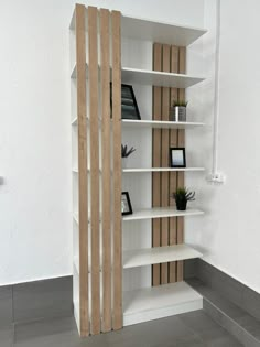 a white bookcase with wooden slats on the front and sides, in an empty room